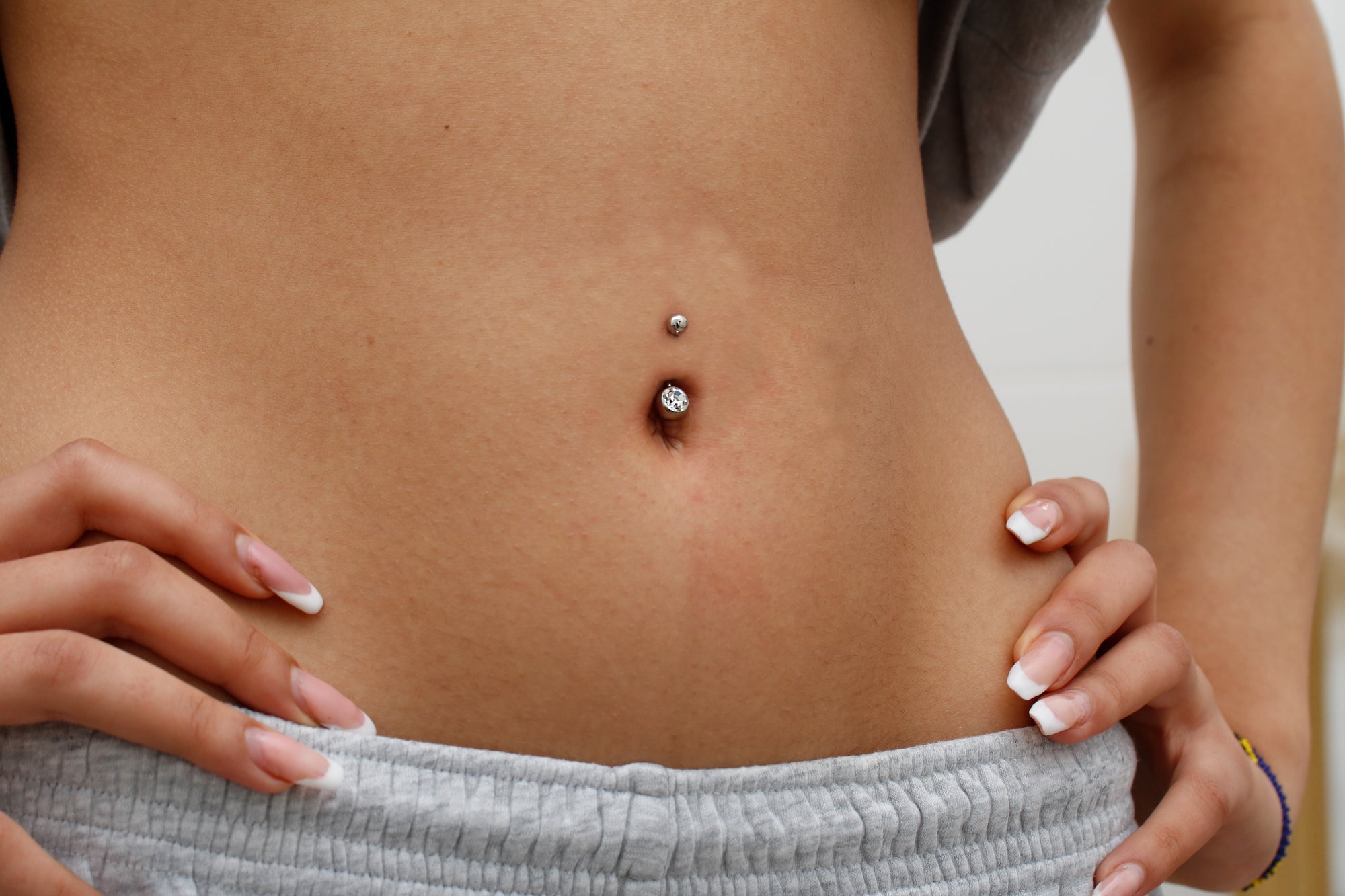 Frau mit klassischem Bauchnabelpiercing aus Titan mit Zirkonia – ROYALSKIN Kollektion